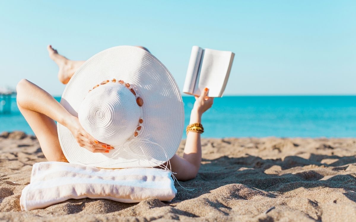 Девушка загорает на пляже с книгой в руках
